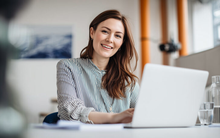Eine Frau am Laptop erstellt zufrieden einen Pressespiegel